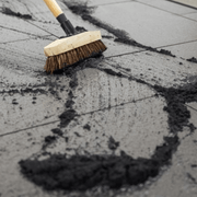 An image of a 12.5kg tub of EasyJoint Select Paving Compound in Jet Black being brushed into gaps in paving slabs