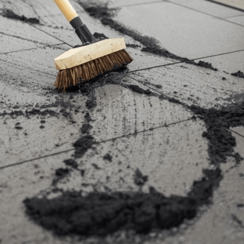 An image of a 12.5kg tub of EasyJoint Select Paving Compound in Jet Black being brushed into gaps in paving slabs