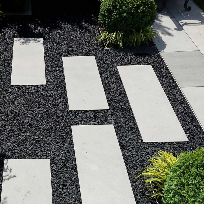 An image of black basalt aggregate stones on a garden with contrasting white slabs to show the finish it gives.