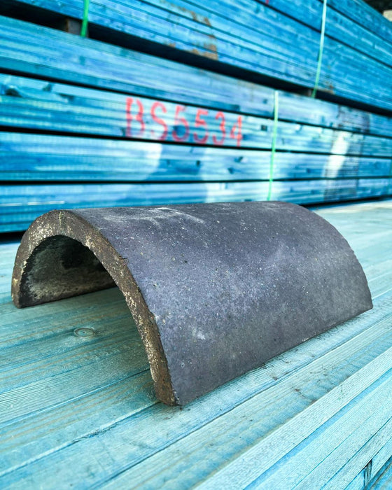 An Image of a Reclaimed Dreadnought Half Round Ridge Tile in the colour Blue. It is a subtle hint of blue on a slate grey base. It is against a Blue timber background.