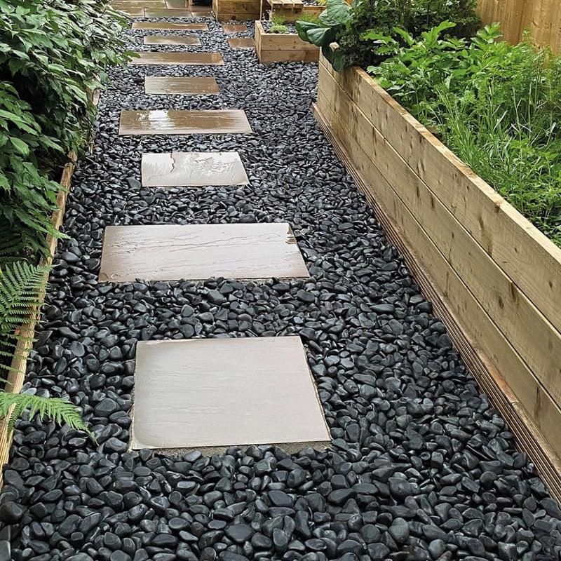 An image showing Ebony Pebble Stone Aggregate Gravel. They are laid as decoration in a garden.