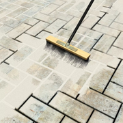 An image of Sika setting sand narrow paving joint filler being swept into block paving gaps with a broom.
