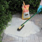 Person using a push broom on a block paved area using Sika Setting sand Narrow joint filler to fill the gaps as grout