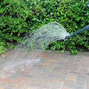 Water being sprayed from a garden hose onto a paved surface to finish and set the Sika Setting Sand Narrow Joint Filler