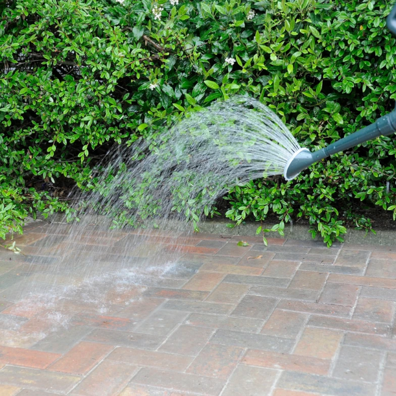 Water being sprayed from a garden hose onto a paved surface to finish and set the Sika Setting Sand Narrow Joint Filler