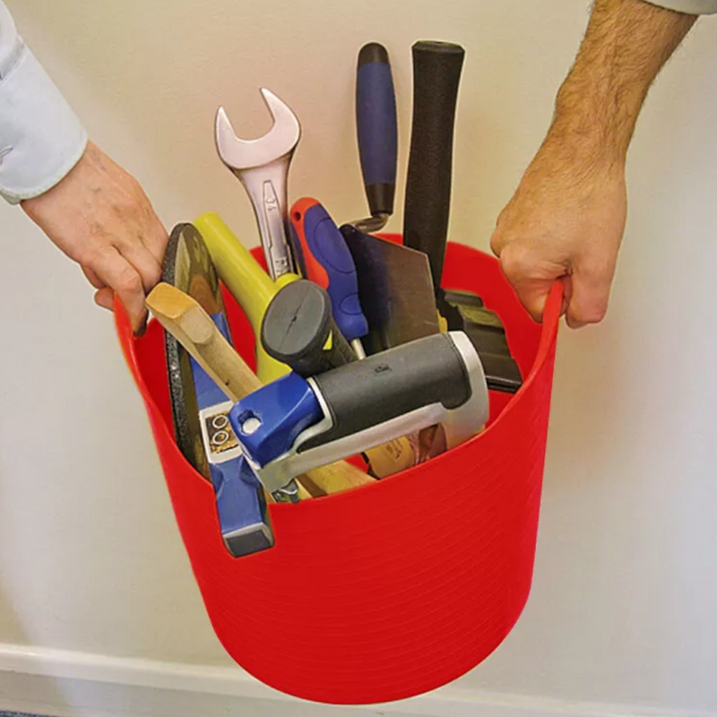 An image showing a Flexible Tub / Bucket. It is Red and is being used to hold a large number of tools. It is being carried by two people to show how much it can carry.