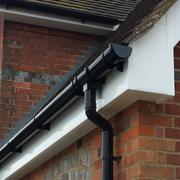 An image of a FreeFoam-Freeflow-112mm-Half-Round-Gutter-Running-Outlet in Black mounted to the eaves of a house to show what it would look like.