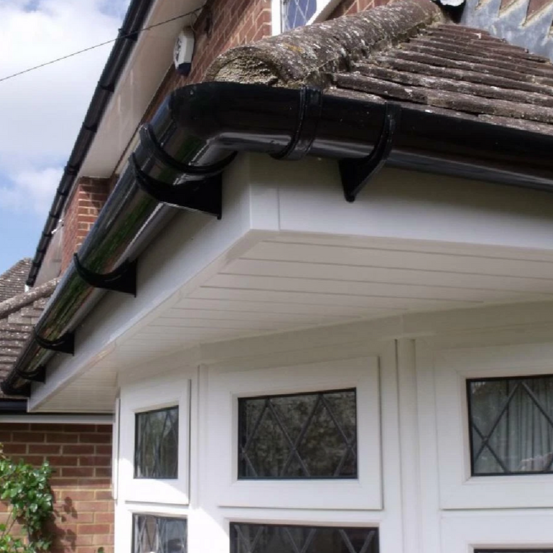 An image of a FreeFoam Freeflow 68mm Half Round Fascia Bracket in Black shown mounted on the facia of a house to show how they look when installed.