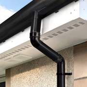 An image of a FreeFoam Freeflow Half Round Offset Bend in Black mounted on the side of a property to show how it looks.
