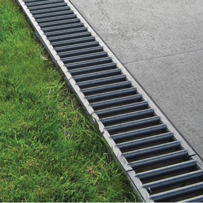 An image of the Galvanised Lid/Grate Garage Drainage Kits. fitted between grass and concrete paving slabs.