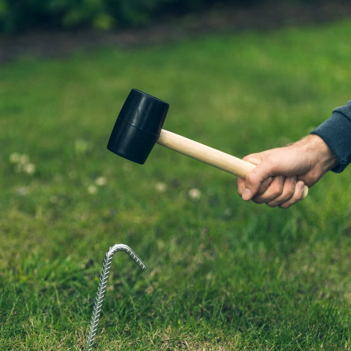 An image of a Rubber Mallet being used to hammer a steel peg into the ground. It has a black rubber head and a robust wooden handle.