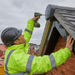 Image of a grey bat box ridge end cap being ftten on the side of a house by a workman with a high viz and a screwdriver.