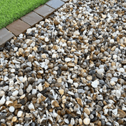 An image of aggregates in the colour Moonstone which are 20mm. They are laid on a patio next to some grass to give an idea of when they look like.