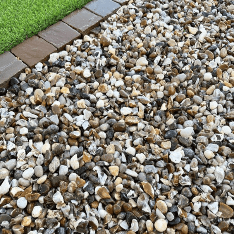 An image of aggregates in the colour Moonstone which are 20mm. They are laid on a patio next to some grass to give an idea of when they look like.
