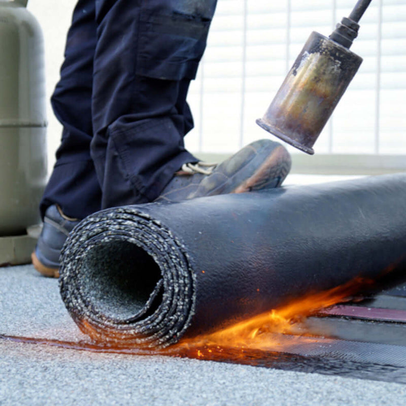 An image of a roll of torch on felt being heated with a flame and rolled onto a roof.