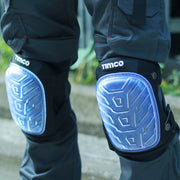 An image of Timco Knee Pads that come in one size. The image shows what they look like fastened onto legs. They are black and have a clear PVC non-slip gel filled pad.