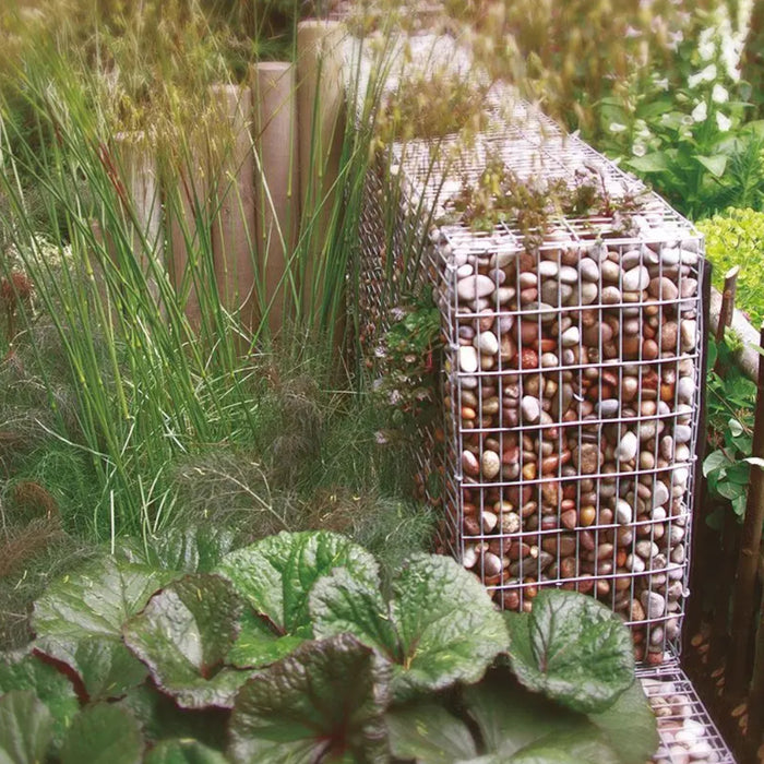 An image showing Tweed Cobble Stone Aggregate. They are piled in a cage as decoration in a garden.