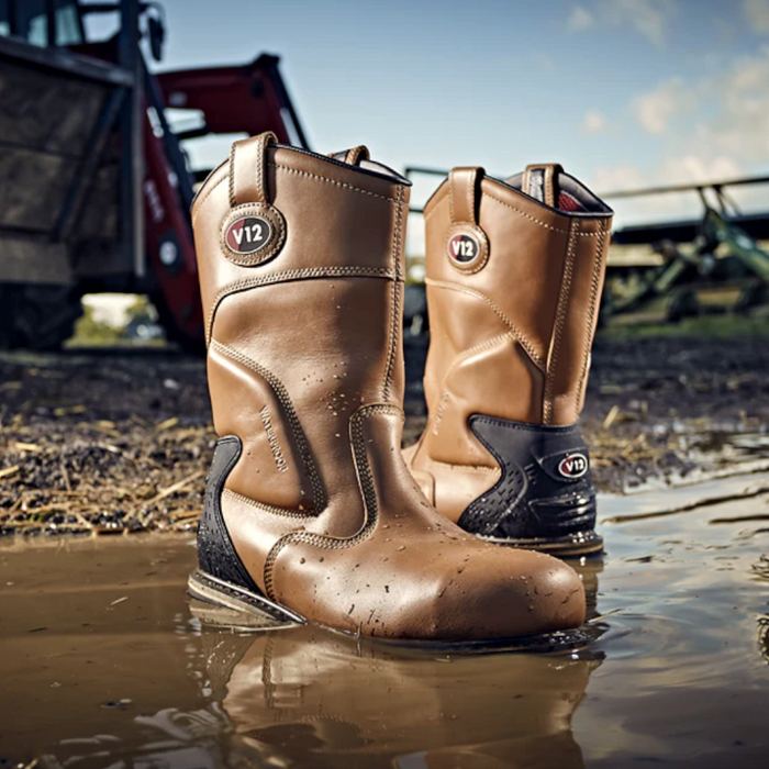 An image of a V12 Tomahawk V1250 Waterproof Rigger Boots Sat in water to show that it is waterproof. It is a light tan colour and has a black heel. The photo is taken on a muddy farm.