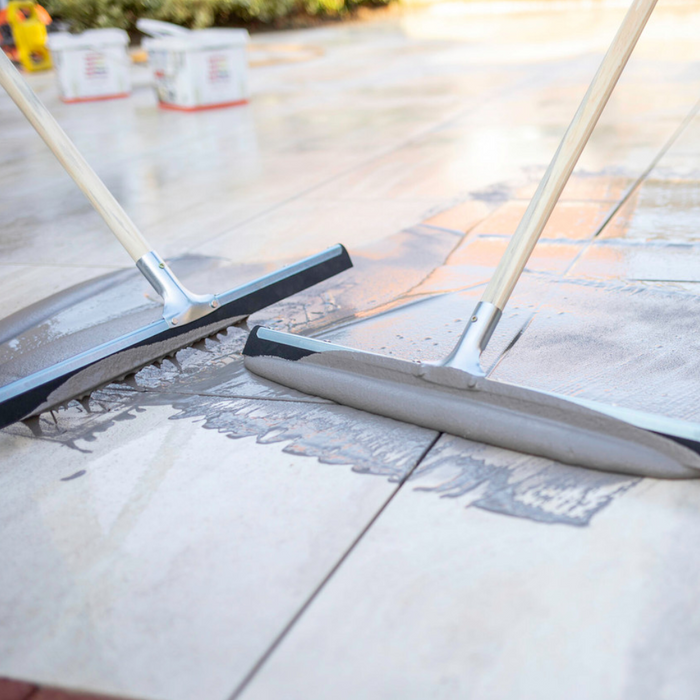 An image of Azpects easy grout porcelain paving slurry being used to fill in the gaps in paving with large squeegees. 